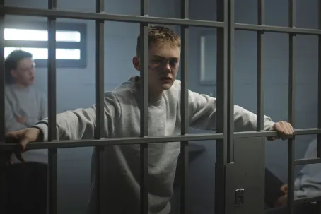 Portrait of diverse teenage prisoners behind metal bars in prison cell looking at camera.