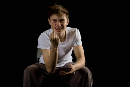 Sitting 17 year old teen boy making a rude gesture with his middle finger