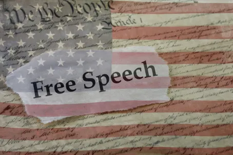 Free Speech news headline on a copy of the United States Constitution and the US flag