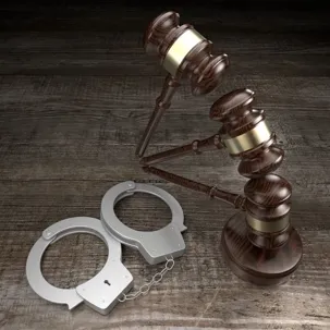 An image of a wooden gavel and handcuffs on a table.