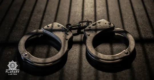 Metal handcuffs placed on a dark wooden surface, symbolizing an arrest or criminal charge.