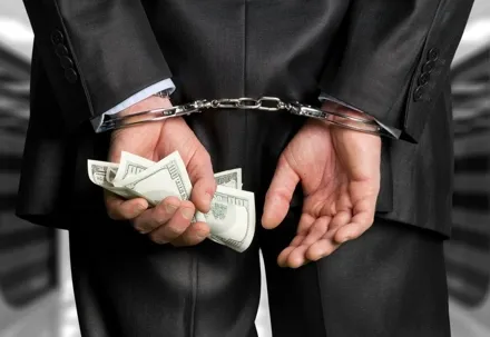 An image of a man under arrest, handcuffed, and holding money.