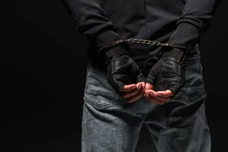 an image of a man wearing black jacket and black gloves arrested with handcuffed