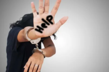 An image of a woman with handcuffs on her hands, asking for help written on her right hand.