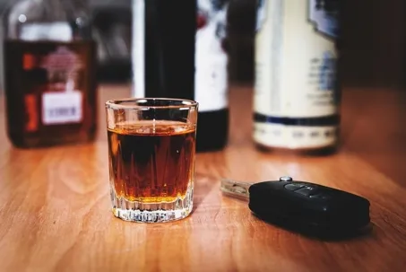 An image of a glass of alcohol and keys on a table.