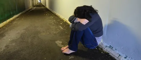 An image of a girl sitting in a hallway, hunched over with her head covered.
